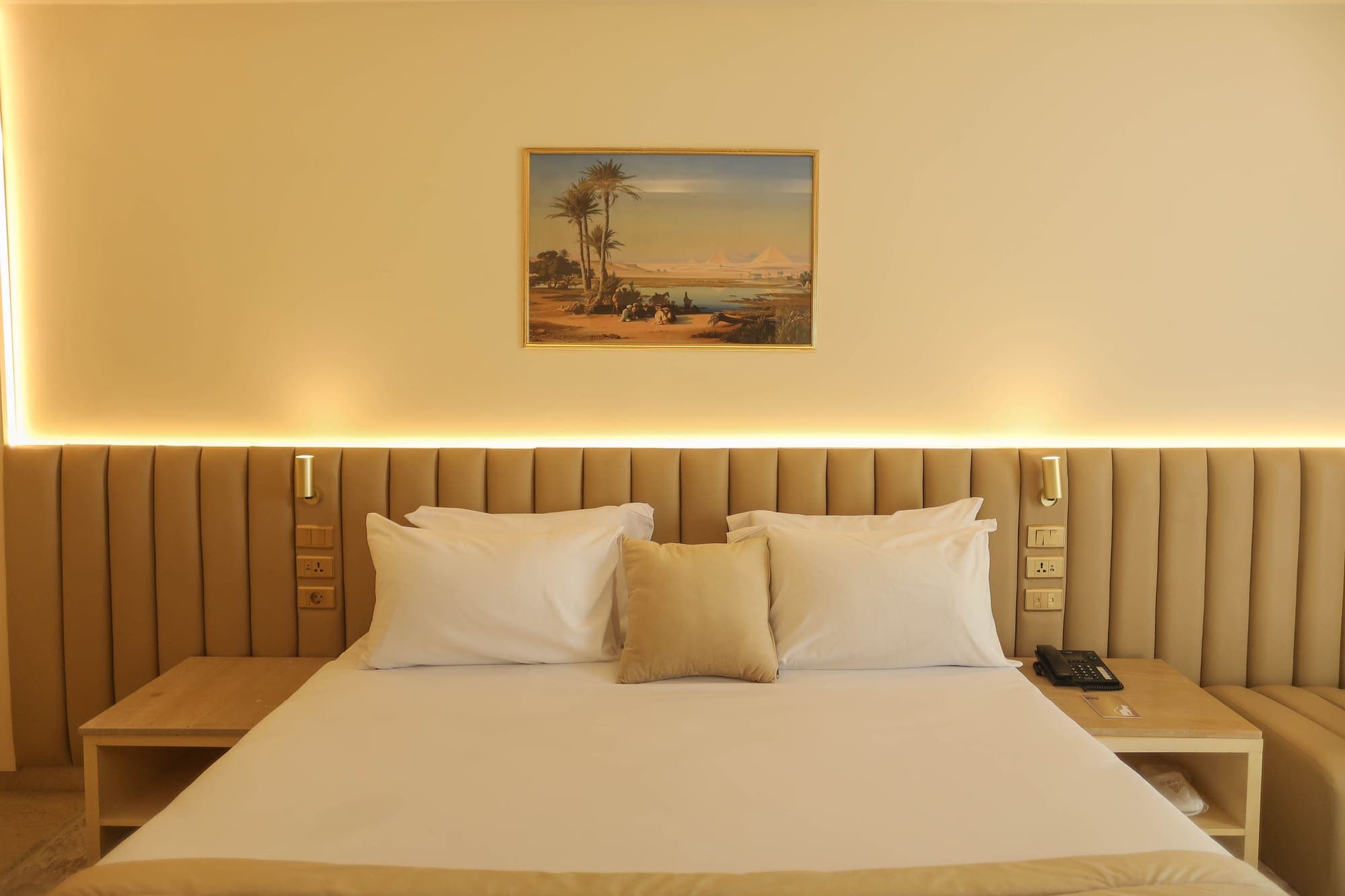 A guest bed with a framed painting of the pyramids above it